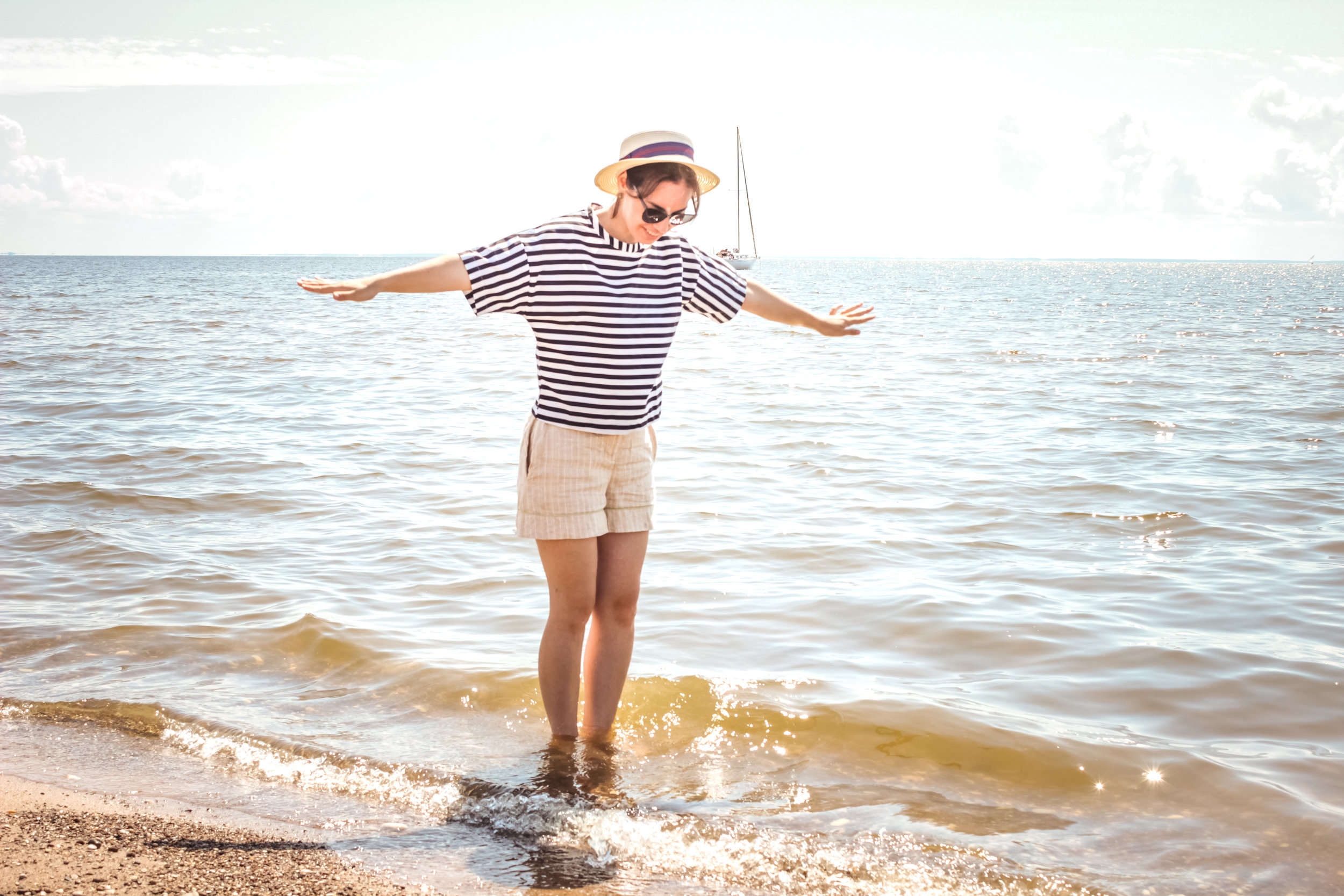 A young women, dressed in loose clothing avoiding heat rash, where the water meets the sand