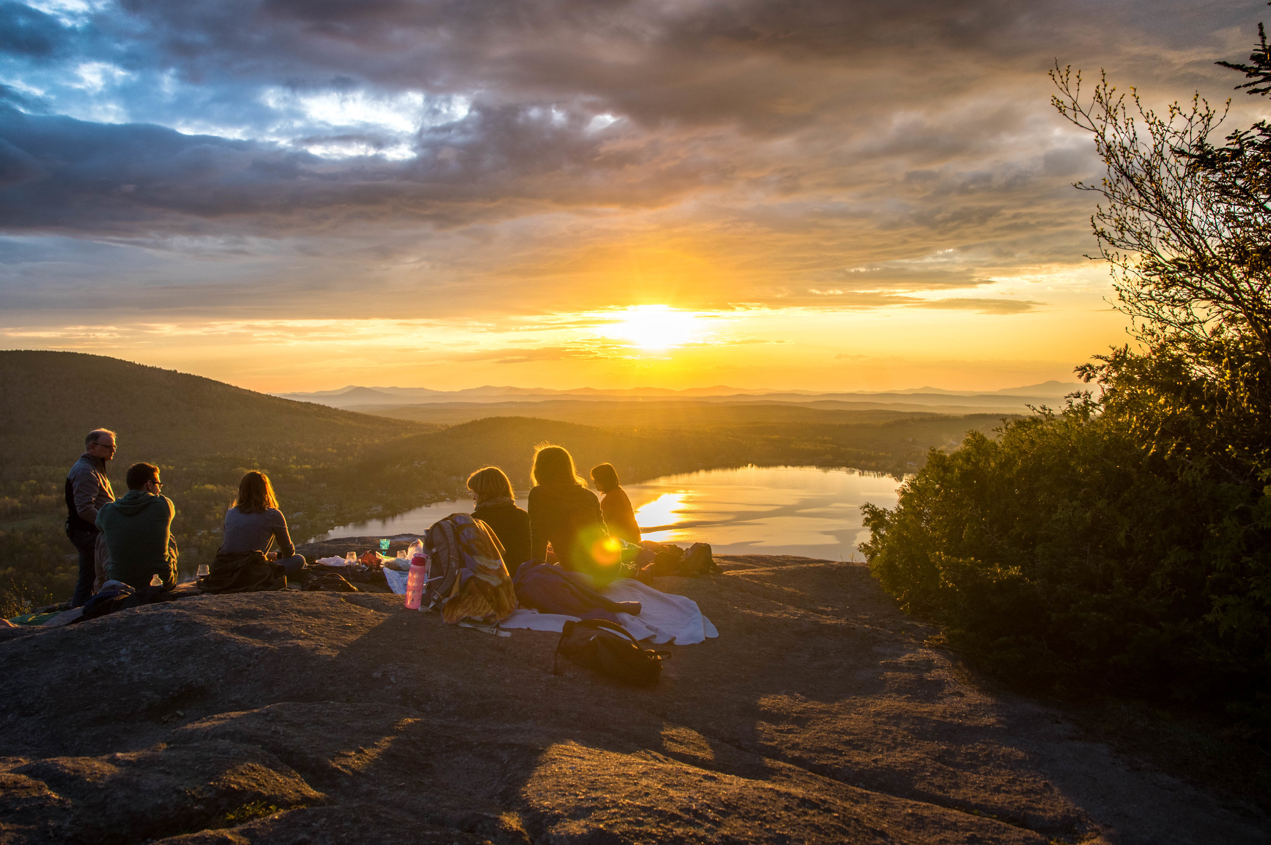 A group of people gathered on a hill at sunset, enjoying an evening activity