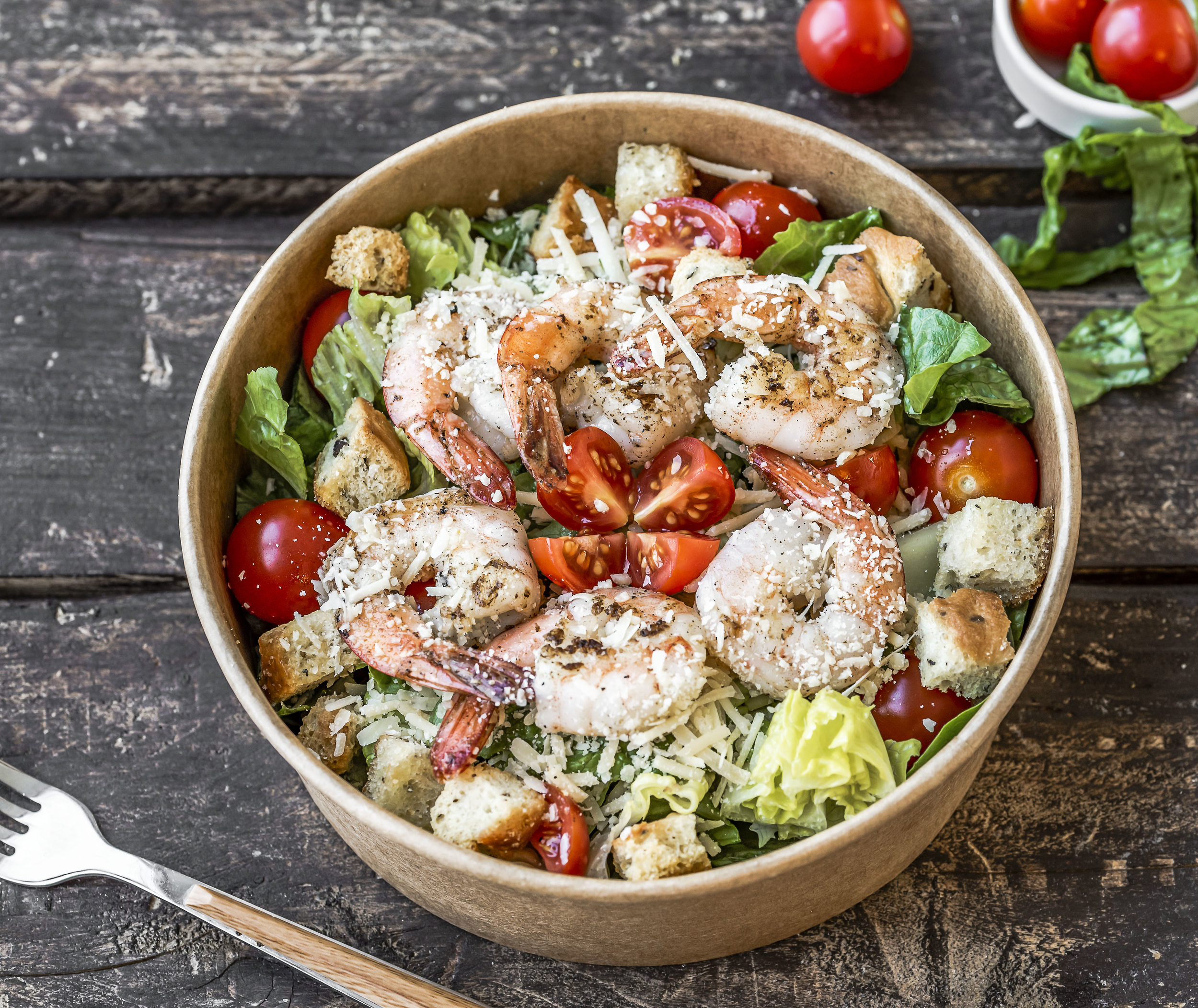 Fresh shrimp salad in a bowl surrounded by fresh vegetables on a reclaimed wood table