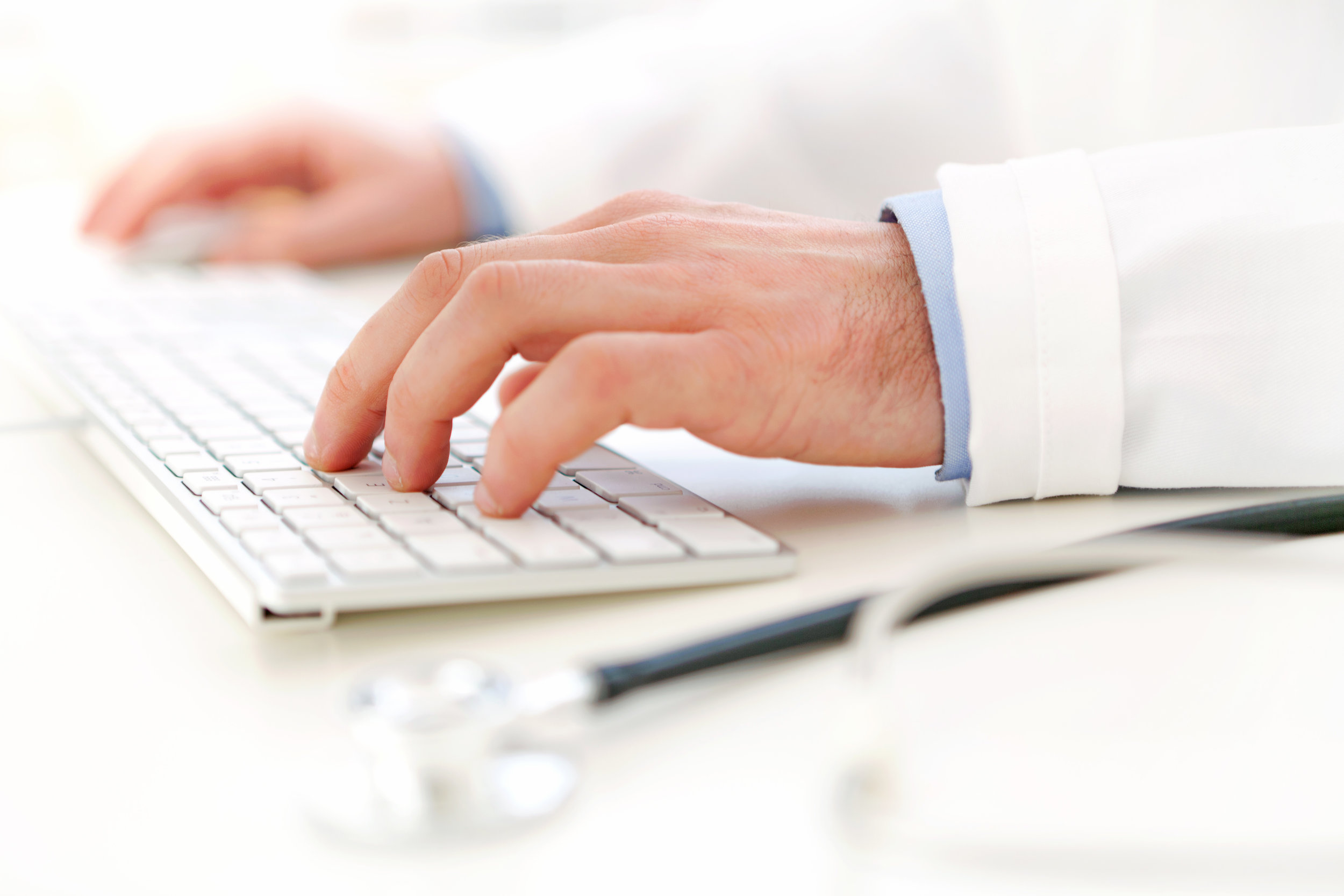 A male doctor typing information into his computer from his keyboard during a patient’s visit