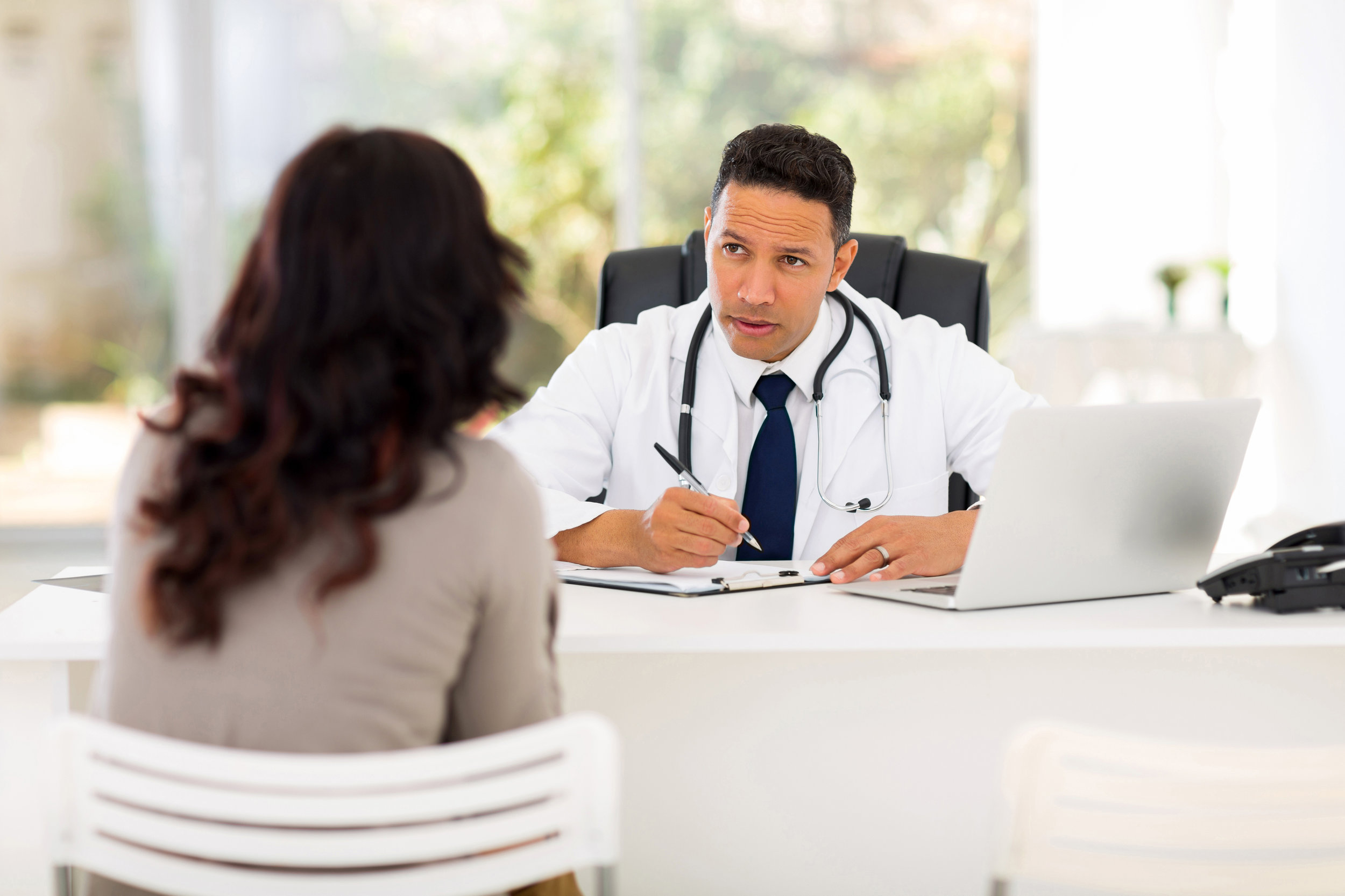Professional medical doctor consulting with female patient in office, encouraging physician patient interaction