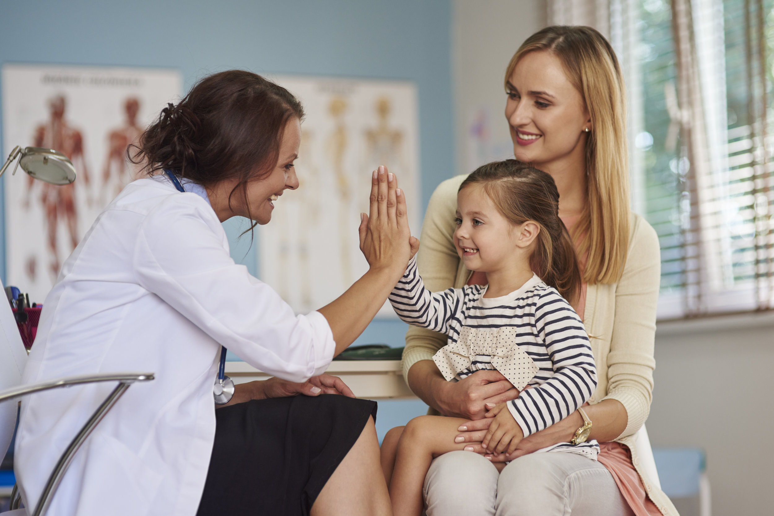 Female family doctor giving a young girl sitting on her mother’s lap a high five