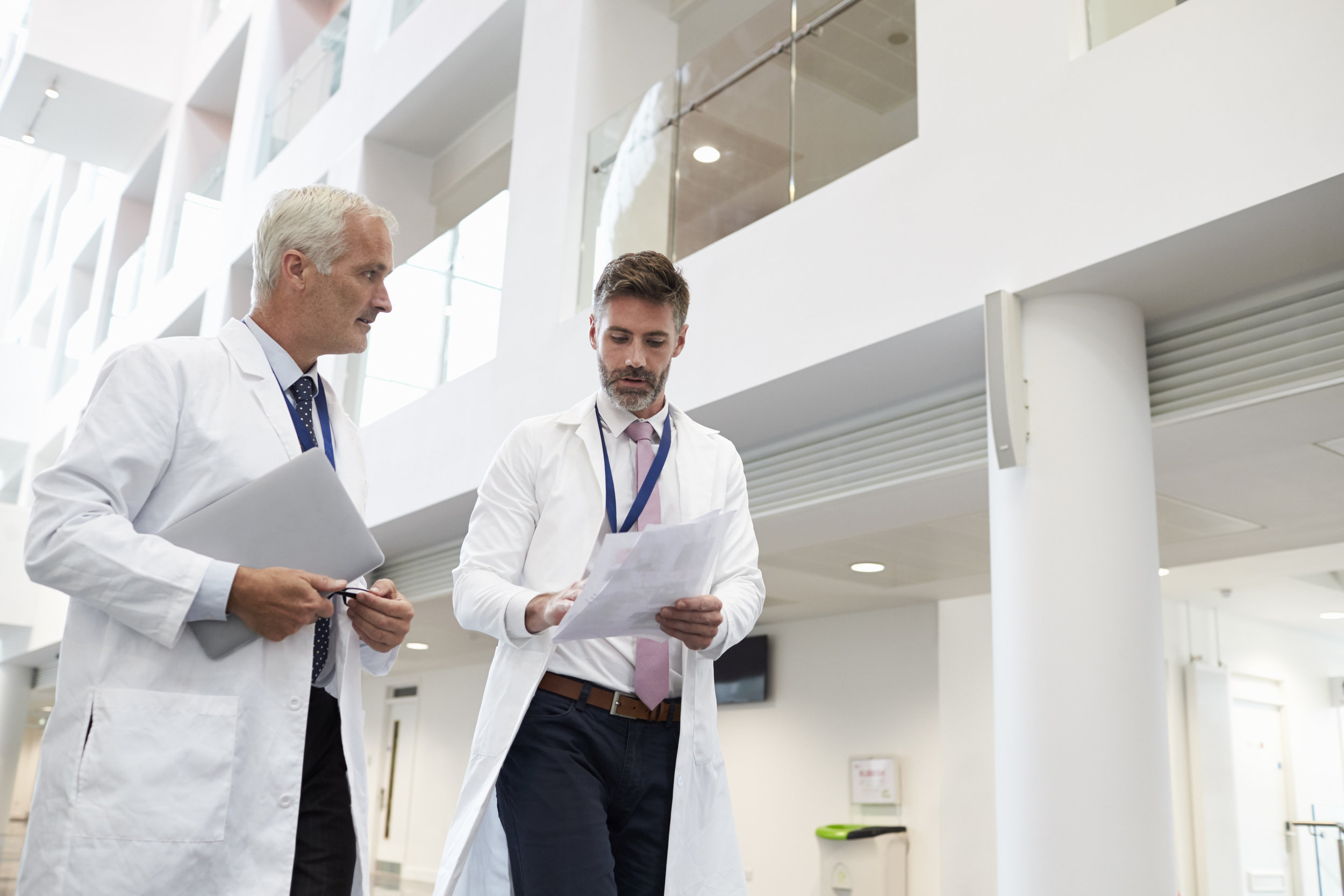 Two doctors discussing patient outcomes as they walk through the halls of a hospital