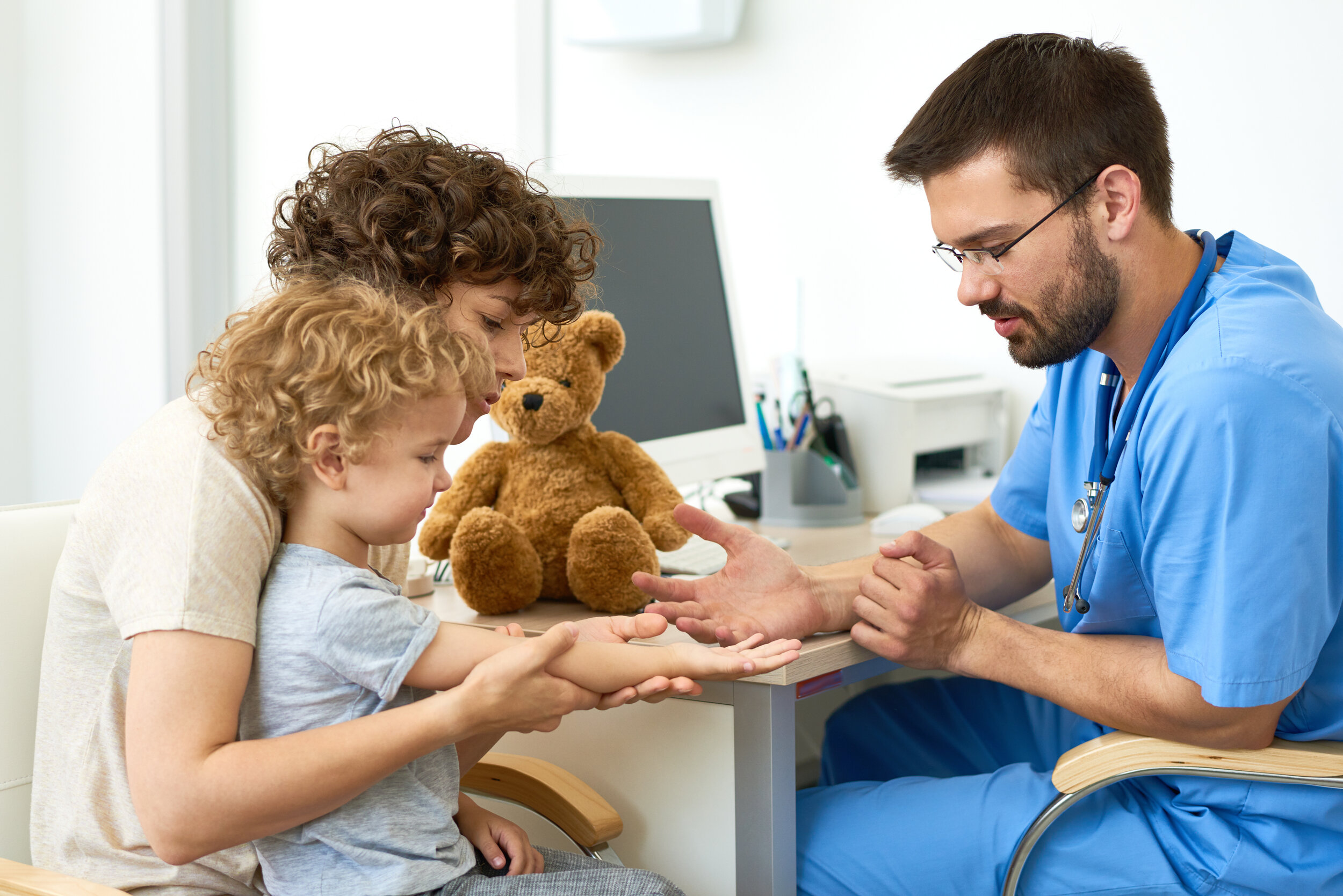Male physician in blue scrubs, examining a young boy’s hand
