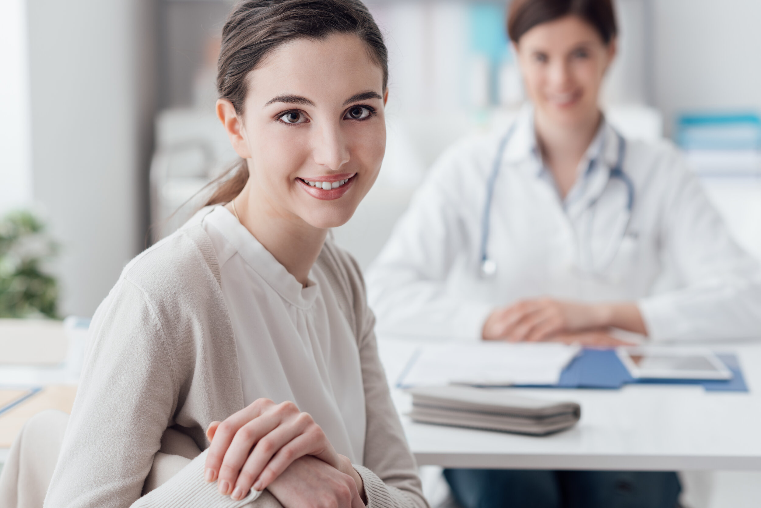 Young female patient smiling while receiving an annual check-up consultation, with a dpc doctor in the background