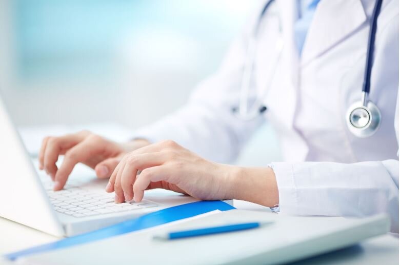 Medical doctor in white coat typing information into a computer