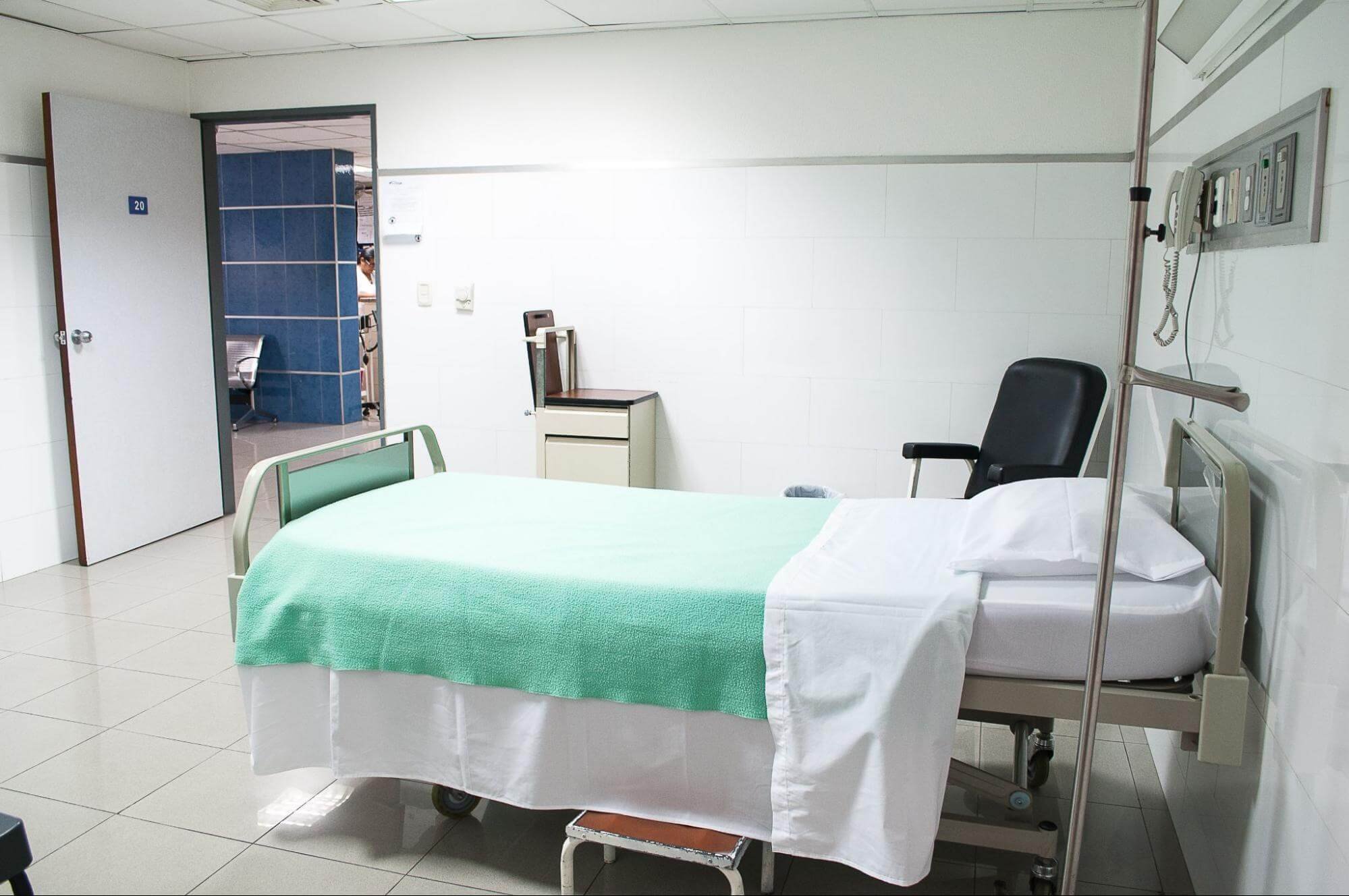 A hospital bed in a white hospital room under a DPC model