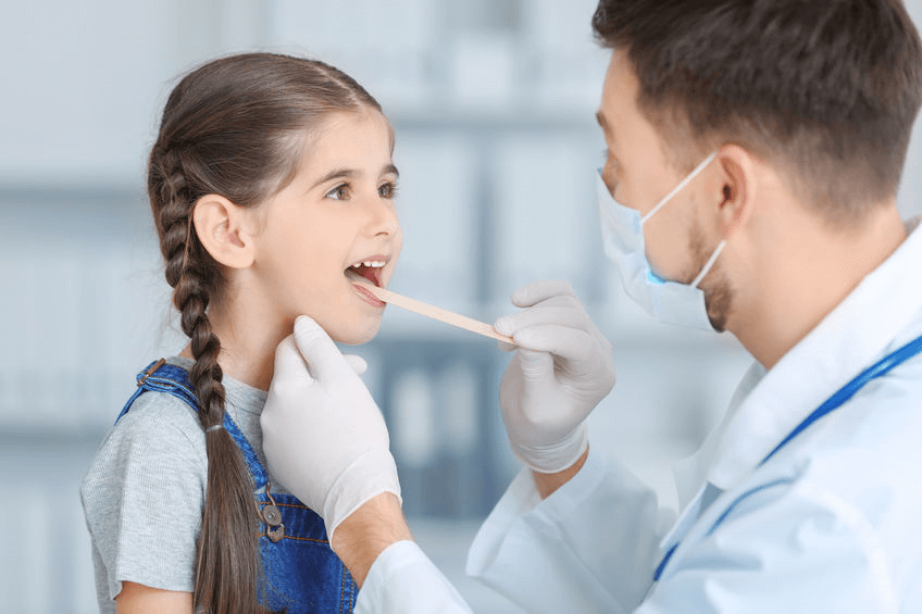 A little girl opens her mouth wide so her family practice doctor can check her tonsils with a popsicle stick