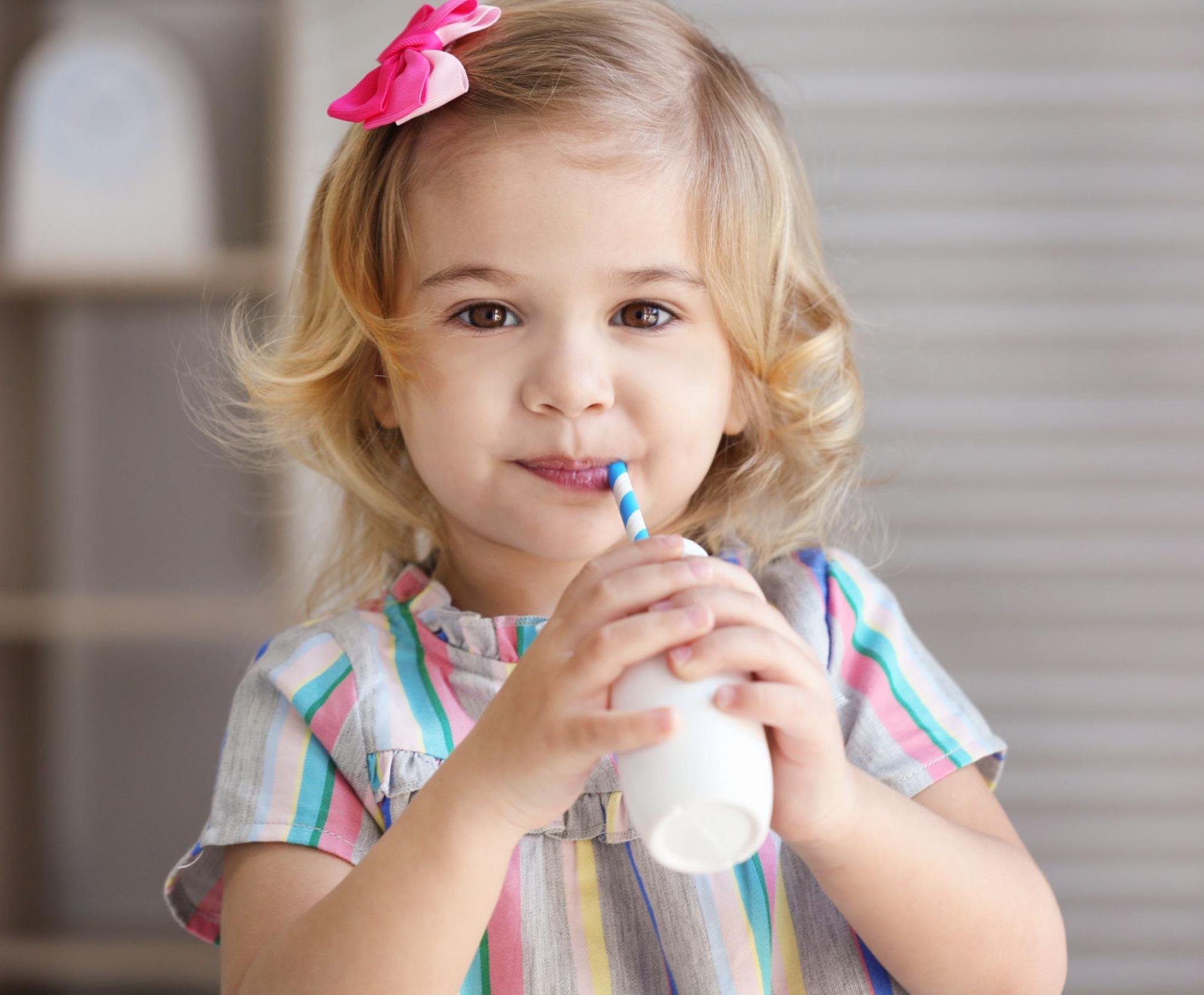 A young girl with blonde hair and a bow drinking milk through a straw