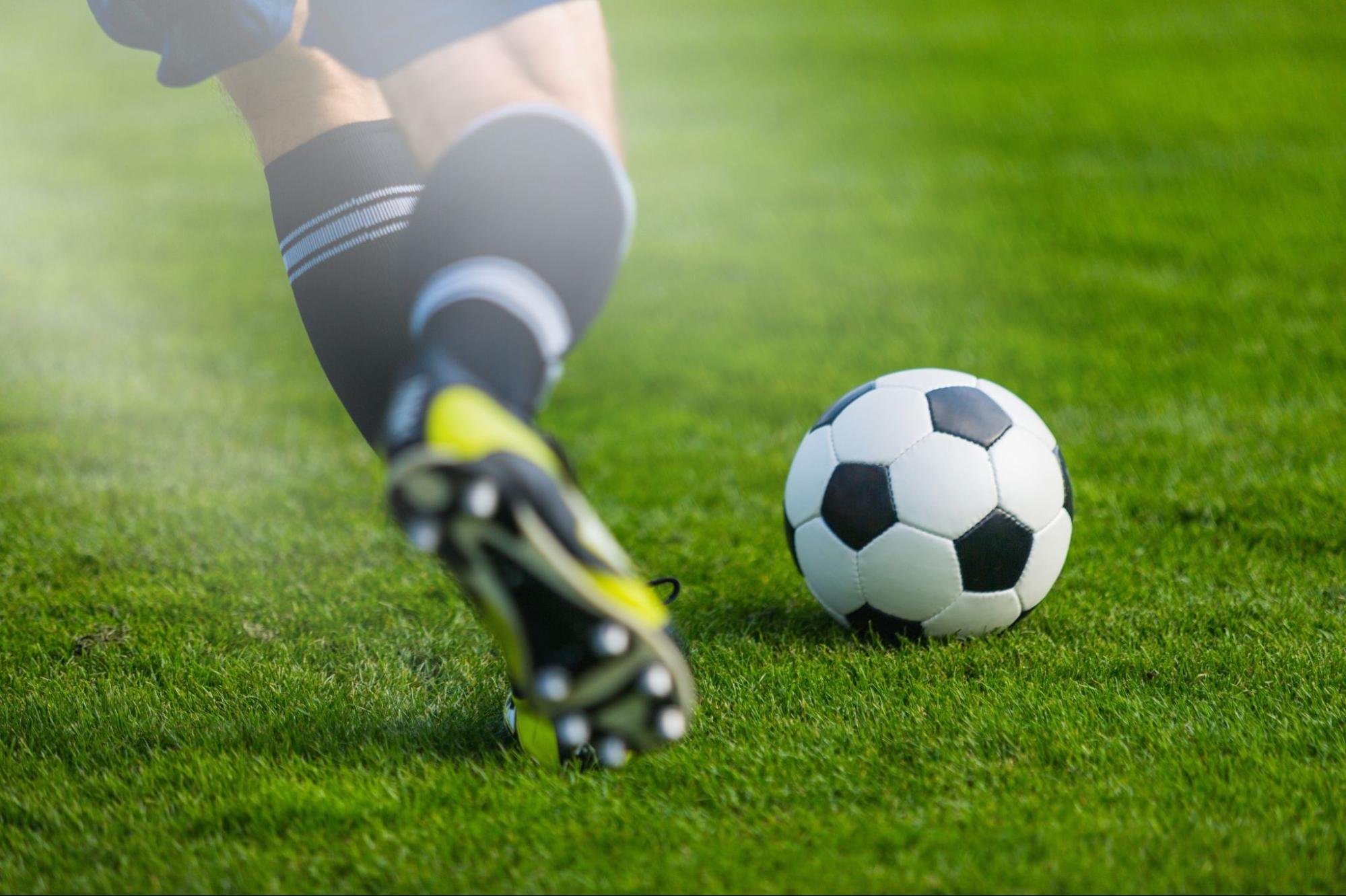 A soccer player wearing socks and cleats kicks a soccer ball on green grass