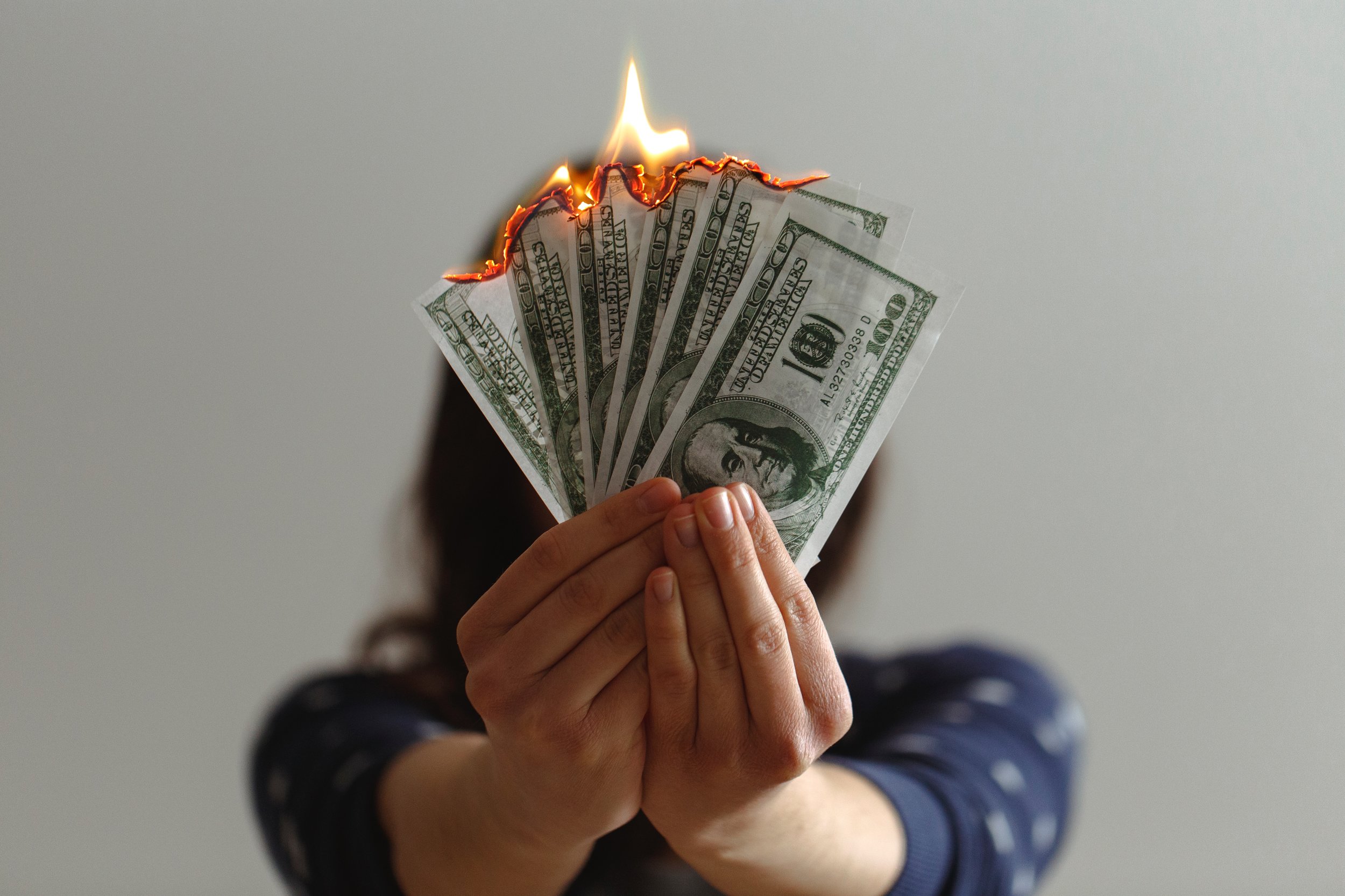 Female in blue shirt holding a fan of dollar bills on fire