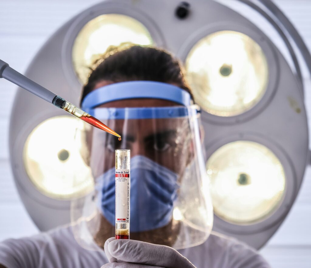 A masked, medical professional analyzing a vial of blood in a lab to assess a patient’s health